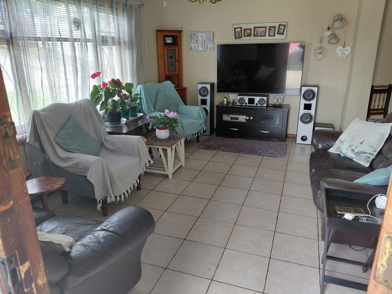 A comfortable living room featuring tiled flooring and a large window with venetian blinds, providing ample natural light.