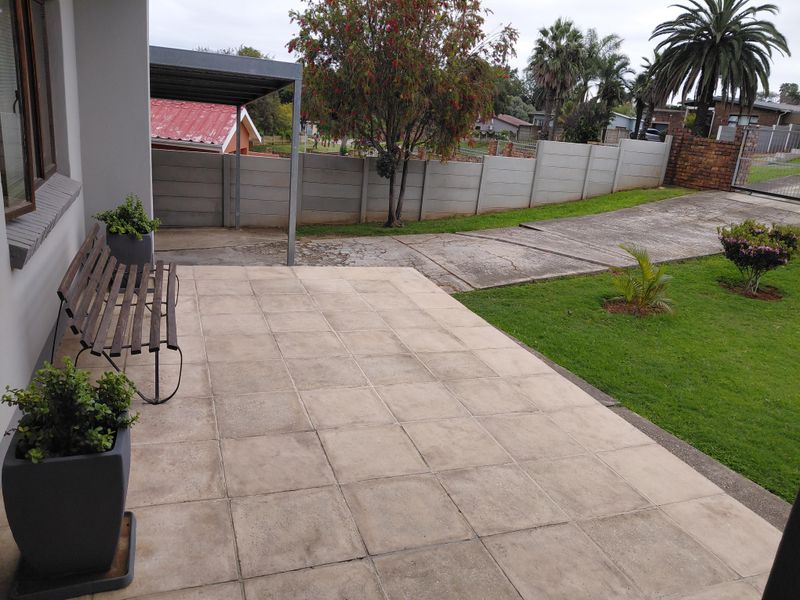 A paved patio area overlooking a garden, featuring a carport and concrete driveway with boundary walling.