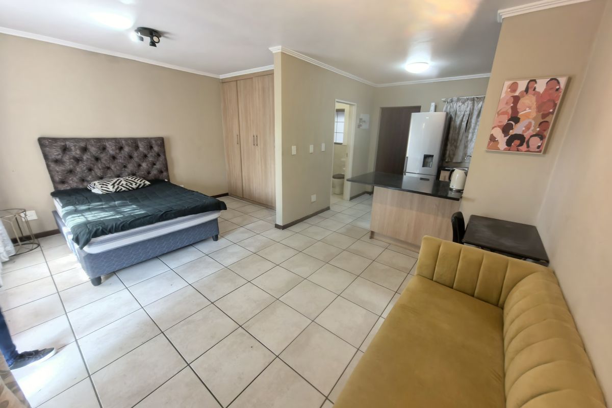 An open-plan studio apartment featuring tiled flooring, built-in cupboards, and a compact kitchen area with a breakfast counter.