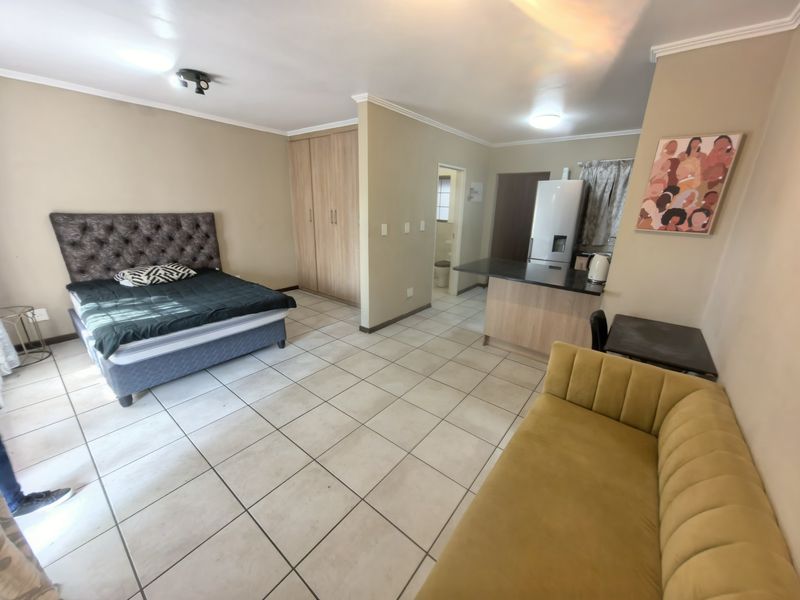 An open-plan studio apartment featuring tiled flooring, built-in cupboards, and a compact kitchen area with a breakfast counter.