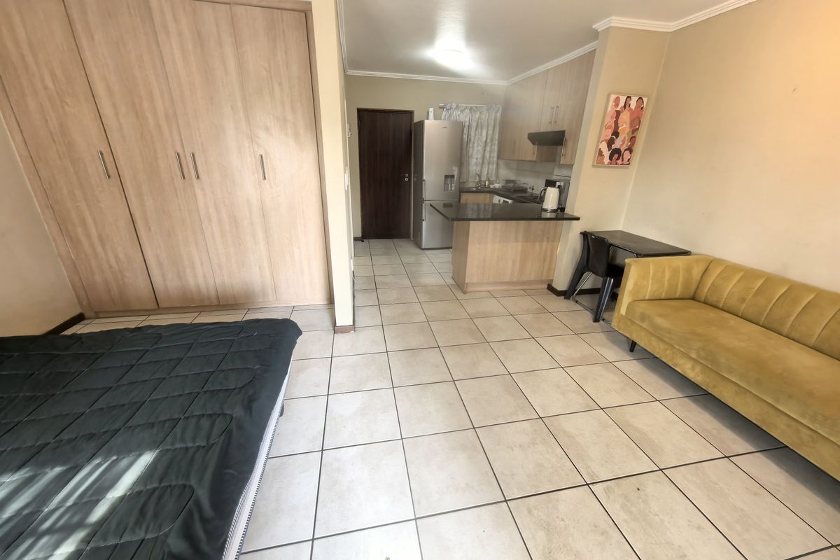 Open-plan studio apartment featuring a compact kitchen with granite countertops, built-in cabinetry, and tiled flooring throughout the living and sleeping area.