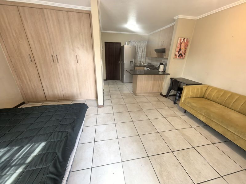 Open-plan studio apartment featuring a compact kitchen with granite countertops, built-in cabinetry, and tiled flooring throughout the living and sleeping area.