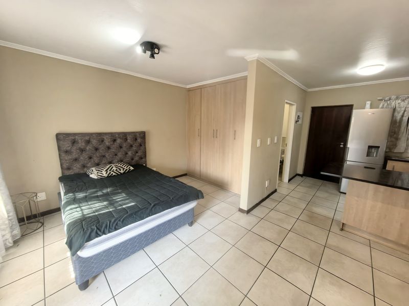 Open-plan studio apartment featuring tiled flooring, built-in bedroom cupboards, and a functional kitchen area with an island.