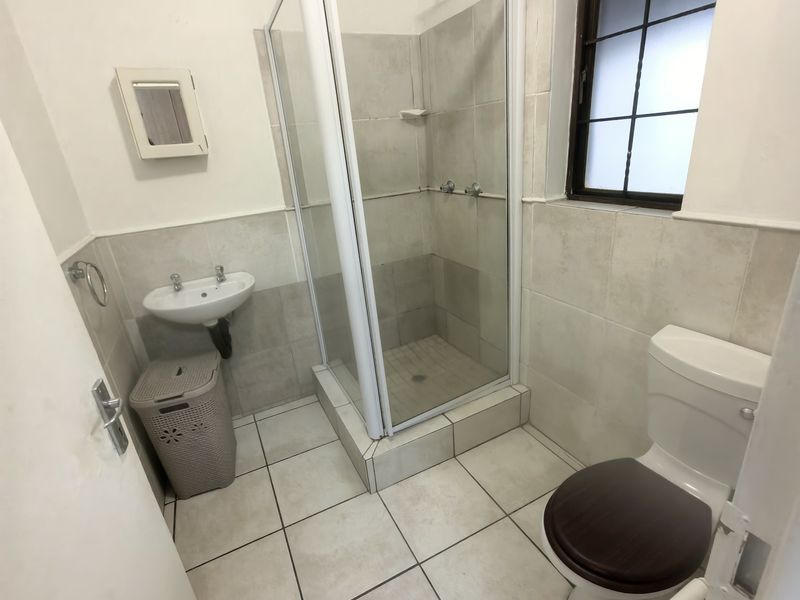 A functional bathroom featuring a shower enclosure, wall-mounted basin, and toilet with neutral floor and wall tiling.