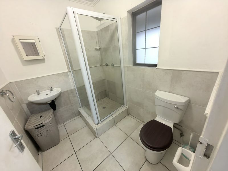 A functional bathroom featuring a shower enclosure, wall-mounted basin, and toilet with neutral tiled finishes and natural light from a window.