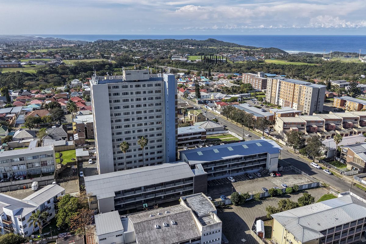 Aerial view of a high-rise residential apartment complex situated in a coastal urban neighborhood with surrounding infrastructure and road access.