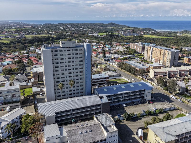 Aerial view of a high-rise residential apartment complex situated in a coastal urban neighborhood with surrounding infrastructure and road access.