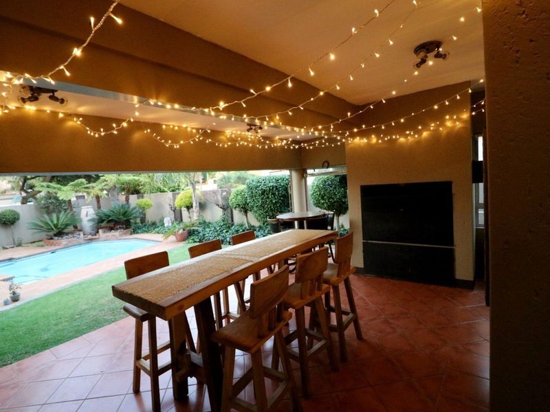Covered outdoor patio featuring a built-in braai, tiled flooring, and direct access to the garden and swimming pool area.