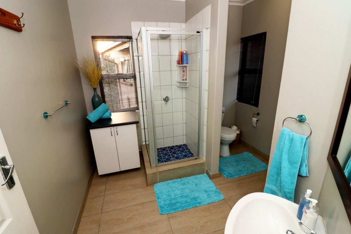 A functional bathroom featuring a tiled shower enclosure, built-in vanity cabinet, pedestal basin, and toilet with neutral wall finishes and tiled flooring.