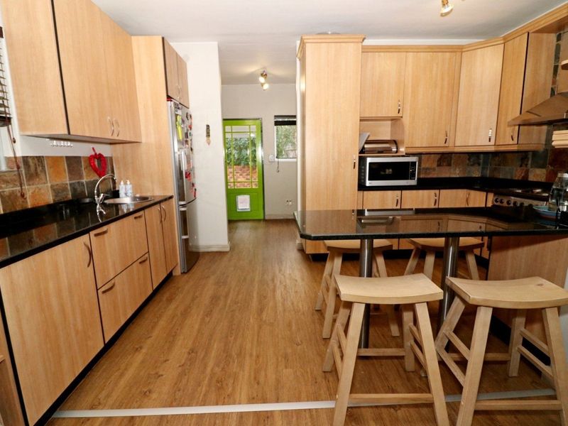 A functional kitchen featuring light wood-tone cabinetry, dark granite countertops, a tiled backsplash, and integrated appliances with a breakfast bar area.