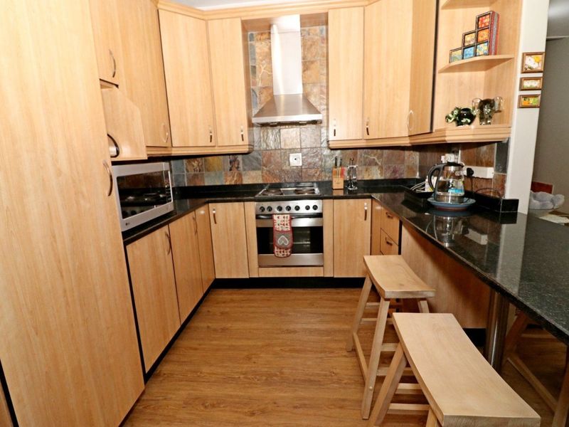 A functional kitchen featuring light wood cabinetry, dark granite countertops, a stone tile backsplash, and integrated stainless steel cooking appliances.