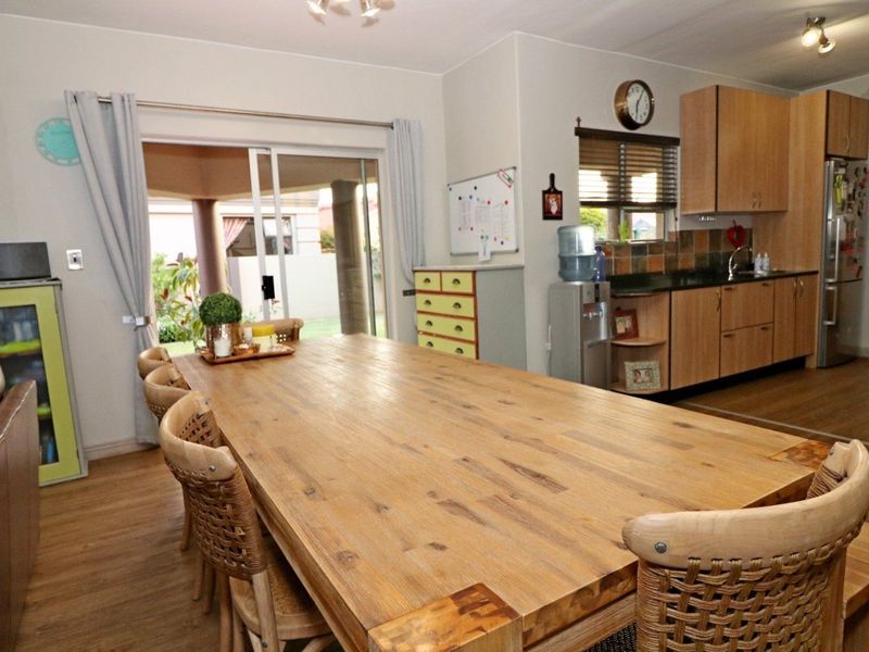 Open-plan living and dining area featuring laminate flooring, built-in kitchen cabinetry with tiled backsplash, and direct access to an outdoor patio through sliding doors.