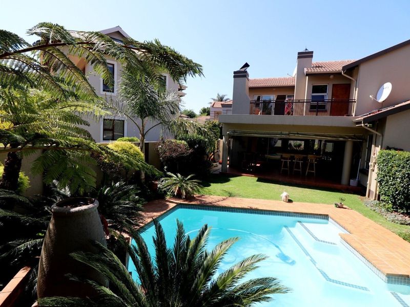 A well-maintained rear garden featuring a swimming pool, tiled surround, covered patio area, and an upper-level balcony overlooking the outdoor space.