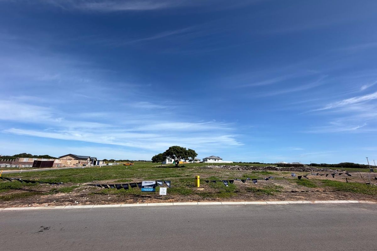 A vacant residential plot of land featuring a paved road frontage and clear views of the surrounding neighborhood.