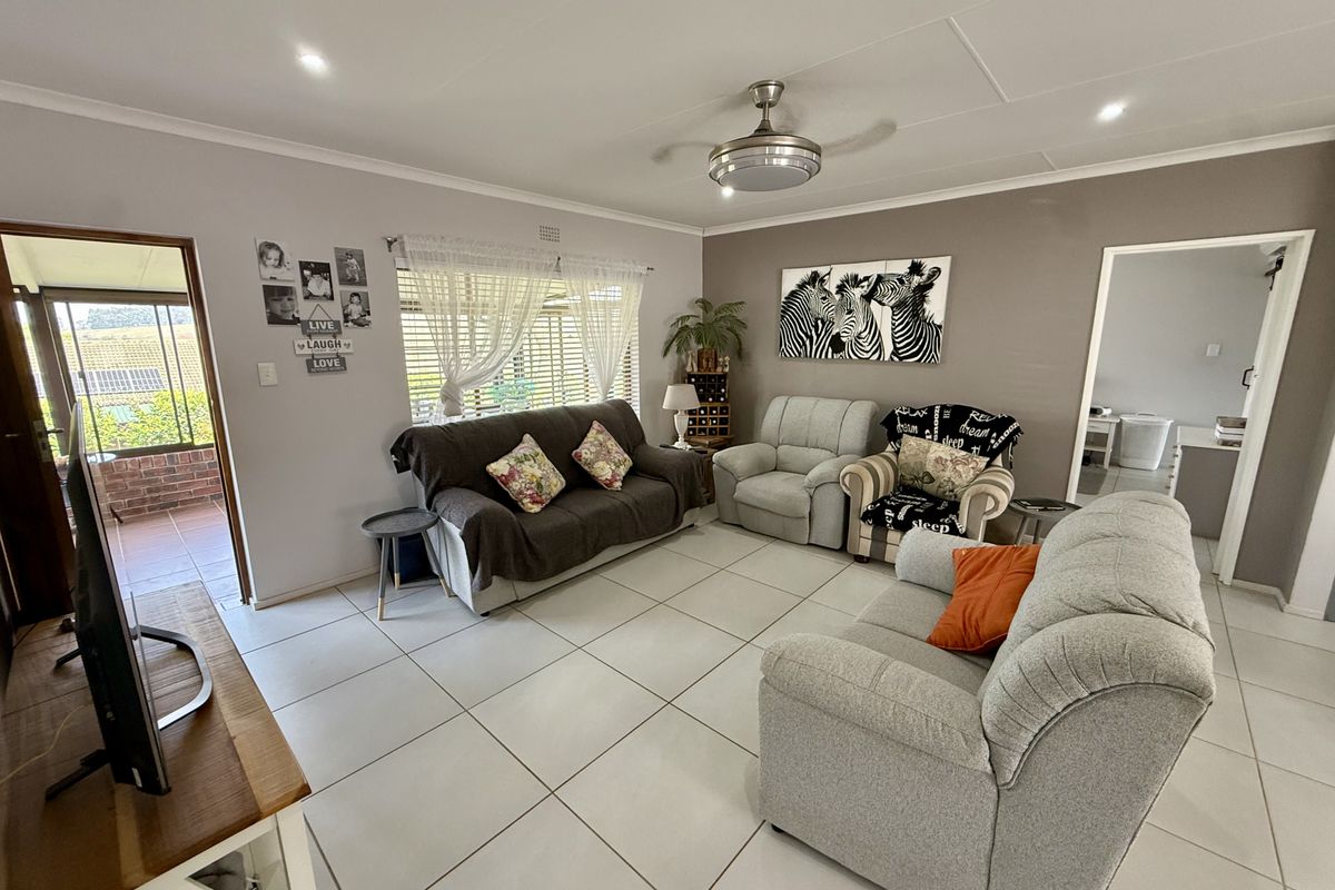 A well-lit living room featuring neutral tiled flooring, a ceiling fan, and direct access to an outdoor patio area.