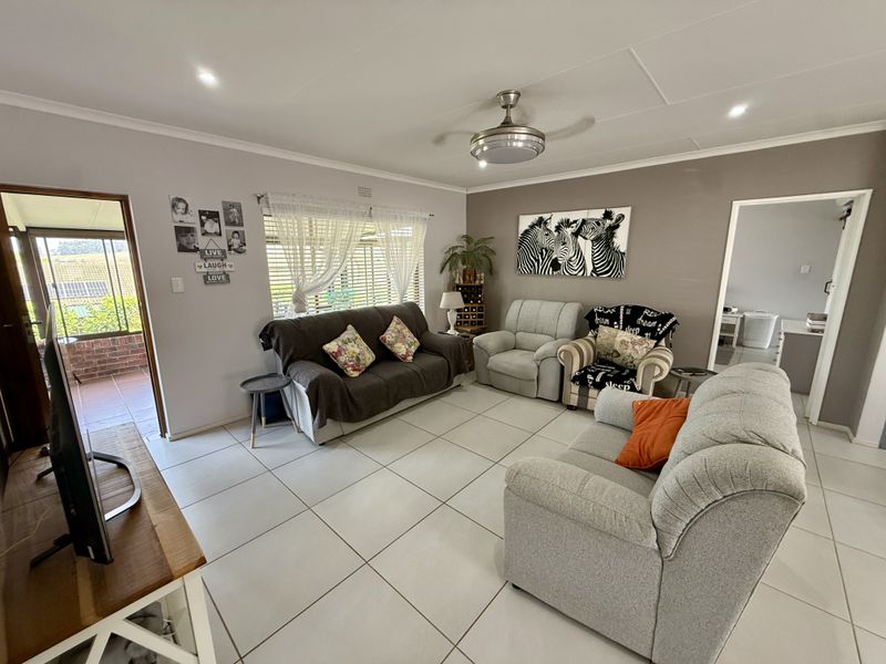 A well-lit living room featuring neutral tiled flooring, a ceiling fan, and direct access to an outdoor patio area.