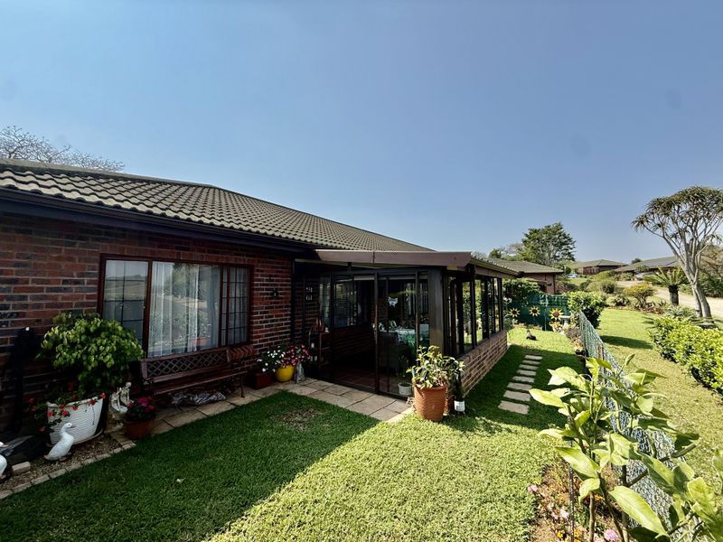 Rear view of the property featuring a brick facade, a tiled roof, and an enclosed patio area overlooking a well-maintained garden.