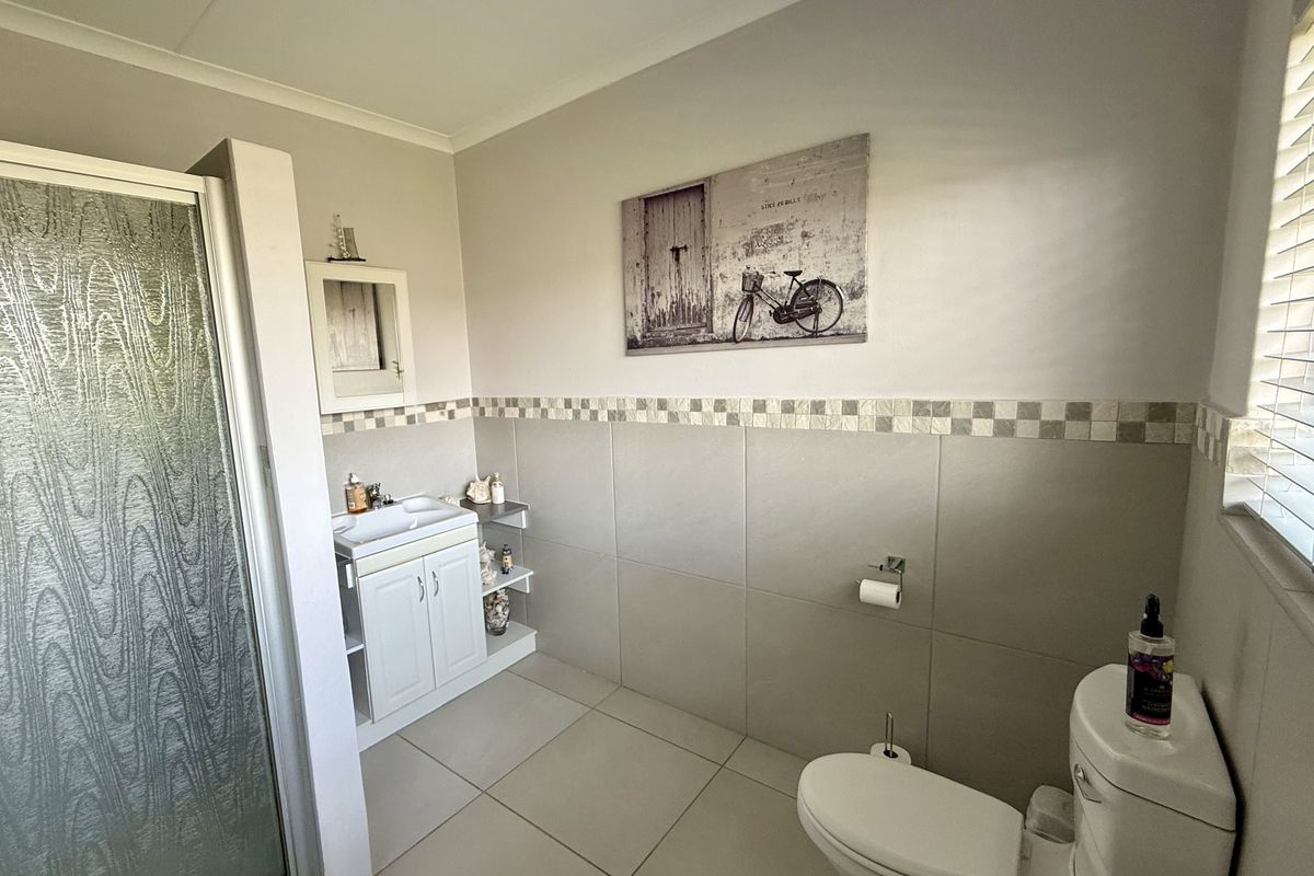 A functional bathroom featuring a shower enclosure, vanity cabinet with basin, and toilet, finished with neutral wall and floor tiling.