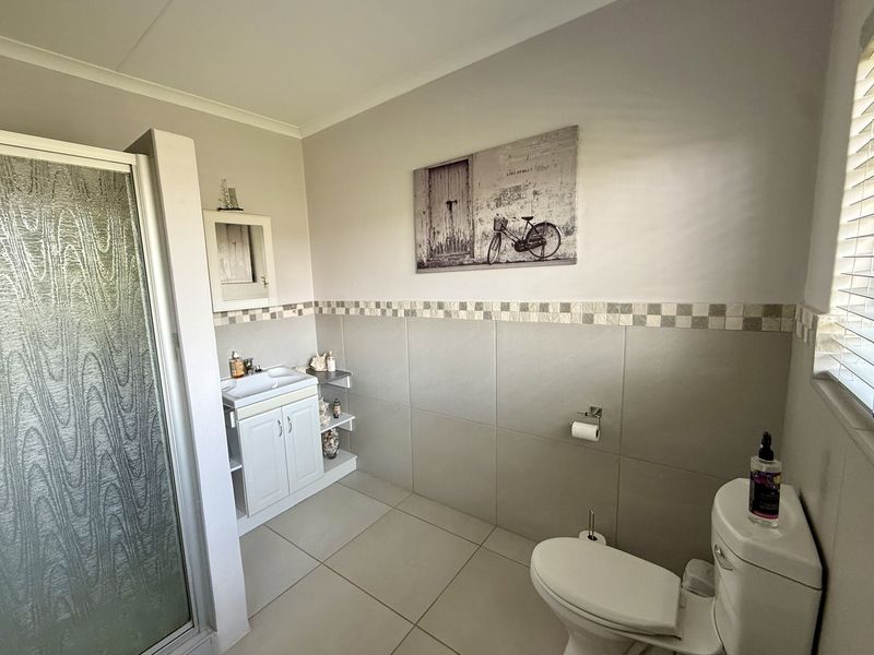 A functional bathroom featuring a shower enclosure, vanity cabinet with basin, and toilet, finished with neutral wall and floor tiling.