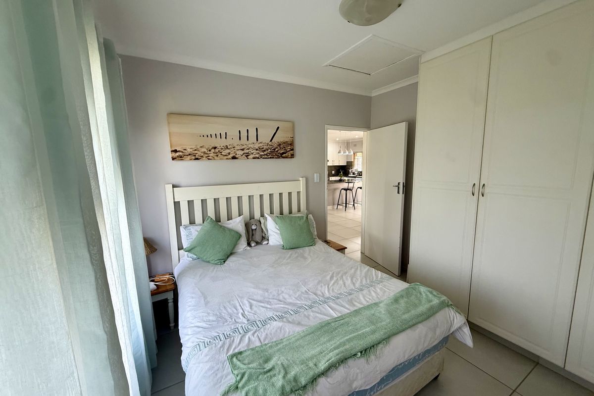 A functional bedroom featuring built-in cupboards, tiled flooring, and a ceiling light fixture, with a view through to the kitchen area.