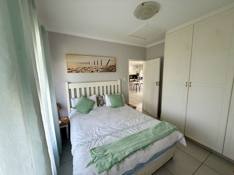 A functional bedroom featuring built-in cupboards, tiled flooring, and a ceiling light fixture, with a view through to the kitchen area.