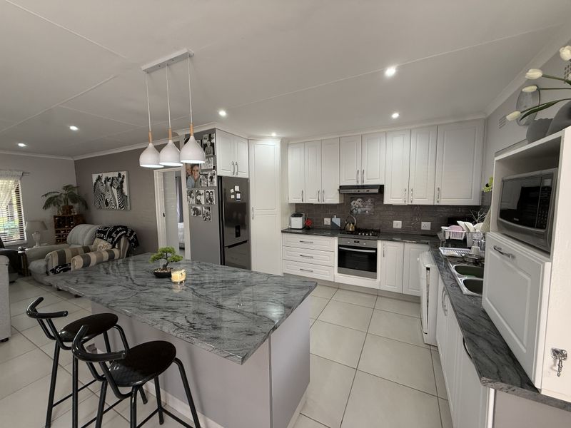 Modern open-plan kitchen featuring a large granite-topped island, white cabinetry, built-in appliances, and recessed lighting, seamlessly flowing into the adjacent living area.