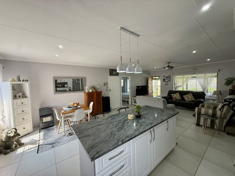Spacious open-plan living area featuring a modern kitchen island with stone countertops, tiled flooring, and recessed lighting, creating a bright and functional living space.