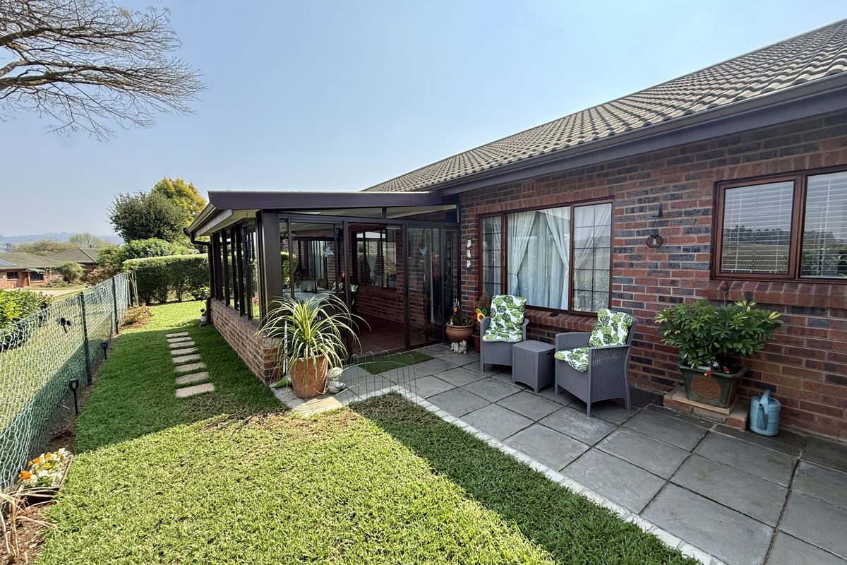 Rear view of the property featuring a brick facade, tiled roof, paved patio area, and an enclosed sunroom extension overlooking the garden.