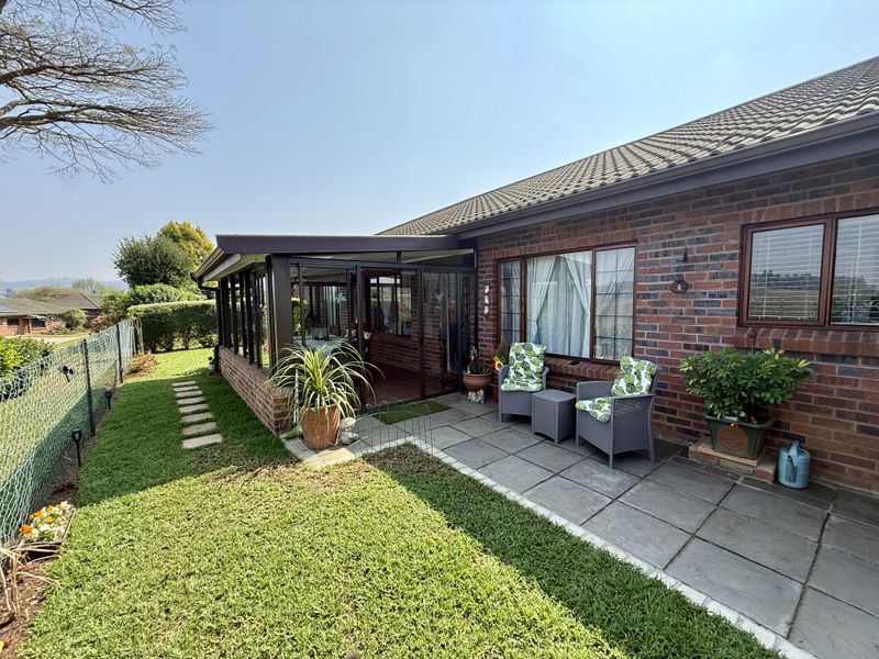 Rear view of the property featuring a brick facade, tiled roof, paved patio area, and an enclosed sunroom extension overlooking the garden.