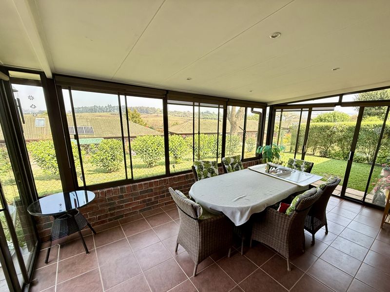A bright, enclosed patio featuring tiled flooring, exposed brick walls, and expansive sliding glass doors offering views of the garden and surrounding landscape.