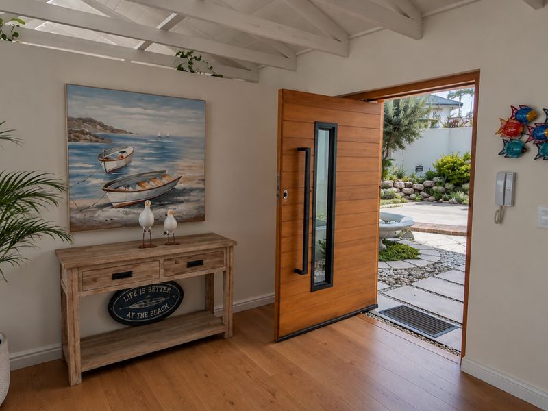 Welcoming entrance foyer featuring a modern timber pivot door, exposed beam ceiling, and warm timber flooring, opening out to a landscaped garden area.