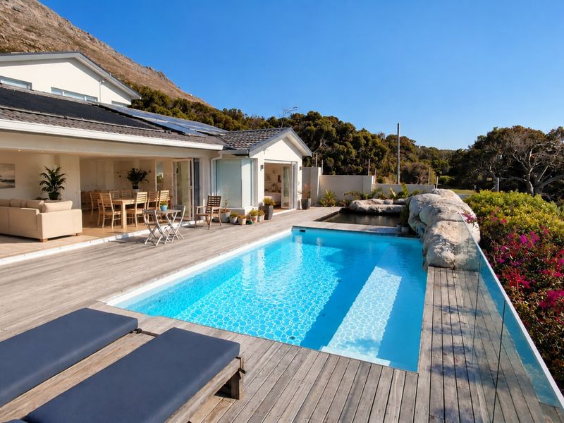 Outdoor pool area featuring timber decking, a glass balustrade, and seamless indoor-outdoor flow through large bi-fold doors into the main living space.