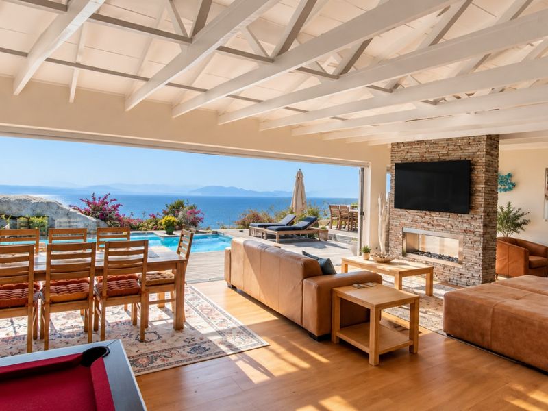 Spacious open-plan living area featuring exposed beam ceilings, a stone-clad fireplace, and seamless indoor-outdoor flow to a deck with a swimming pool and ocean views.