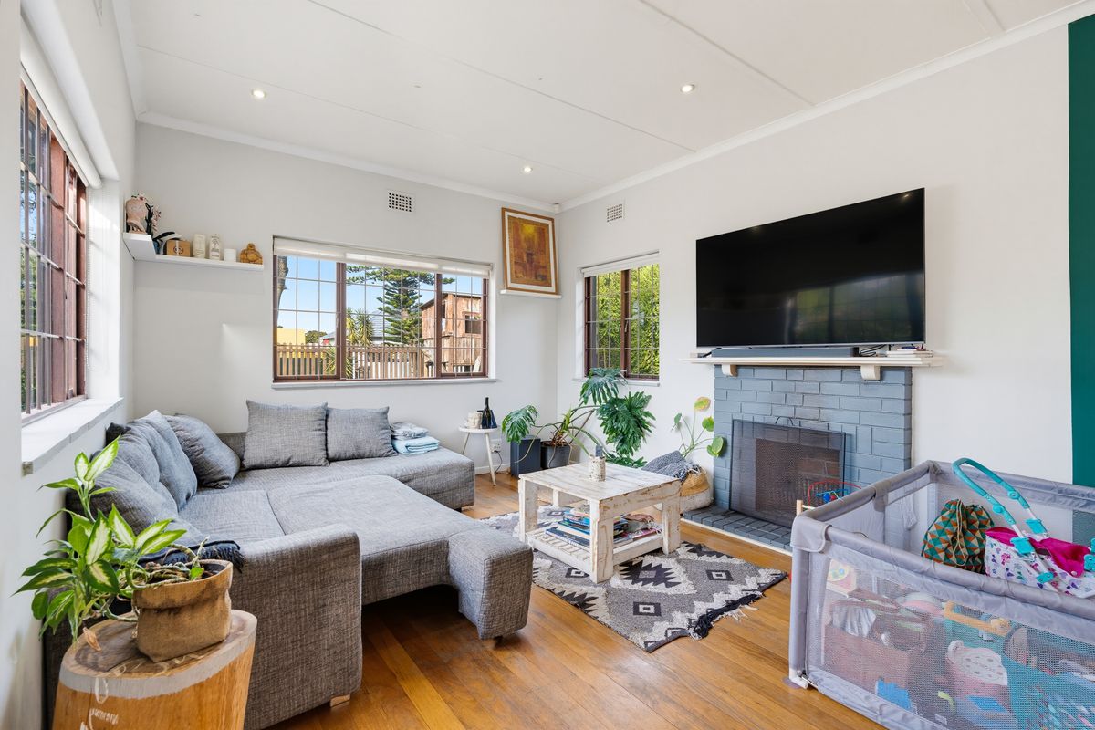 A bright living room featuring hardwood flooring, a painted brick fireplace, and large windows that provide ample natural light.