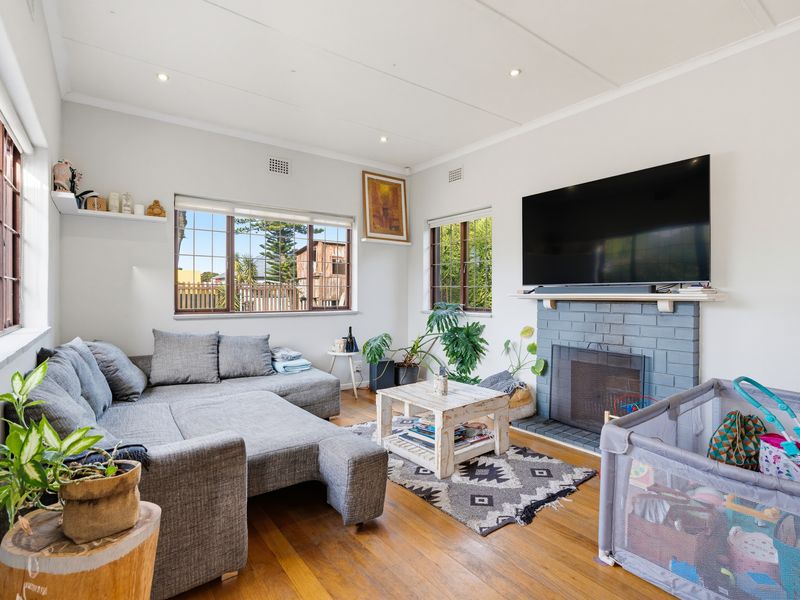 A bright living room featuring hardwood flooring, a painted brick fireplace, and large windows that provide ample natural light.
