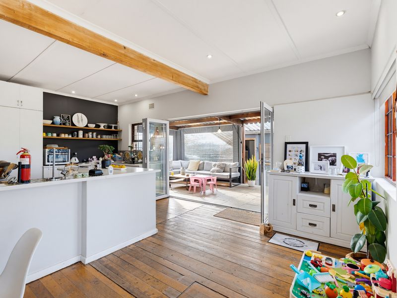 Bright open-plan kitchen and living area featuring timber flooring, exposed ceiling beams, and seamless indoor-outdoor flow through bi-fold doors to the patio.