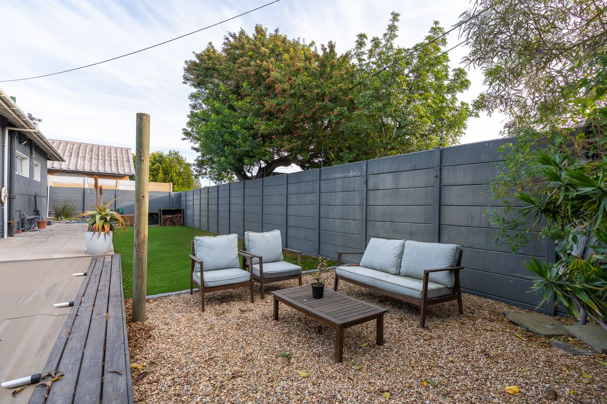 A well-maintained rear garden featuring a gravel seating area, artificial lawn, and a secure precast concrete boundary wall.