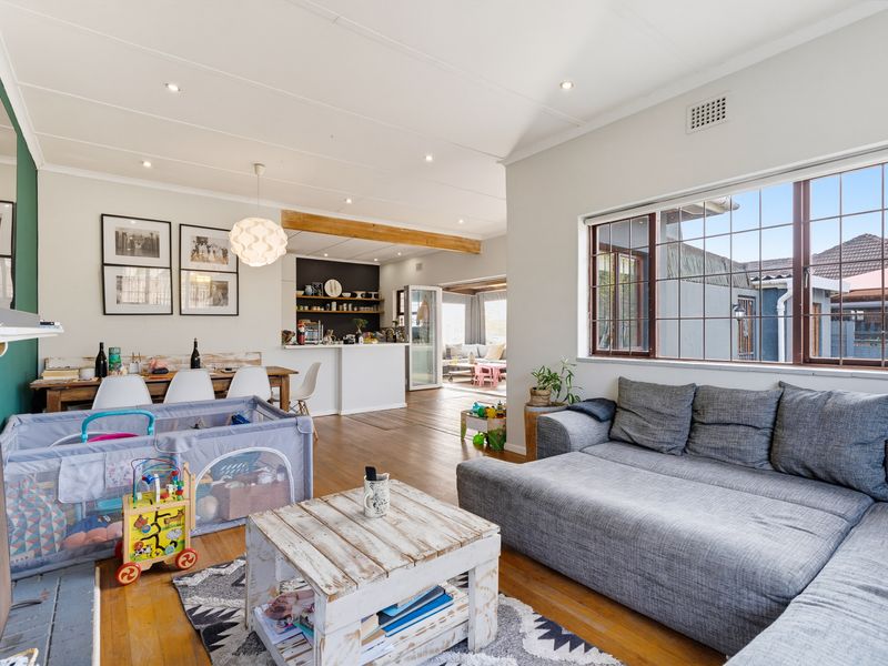 Spacious open-plan living and dining area featuring timber flooring, recessed lighting, and a fireplace, flowing seamlessly into the kitchen and adjacent sunroom.