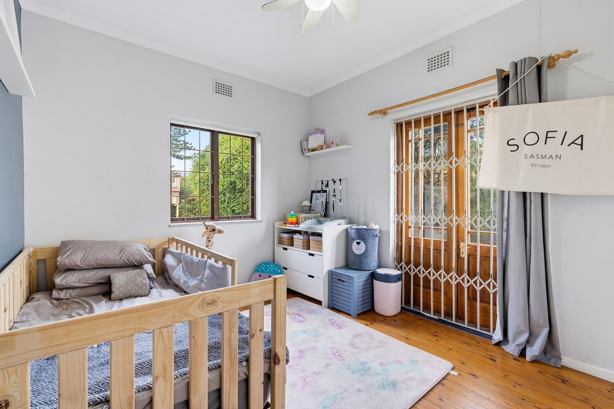 A bright bedroom featuring polished timber flooring, a ceiling fan, and direct access to the outdoors through timber-framed glass doors with security gates.
