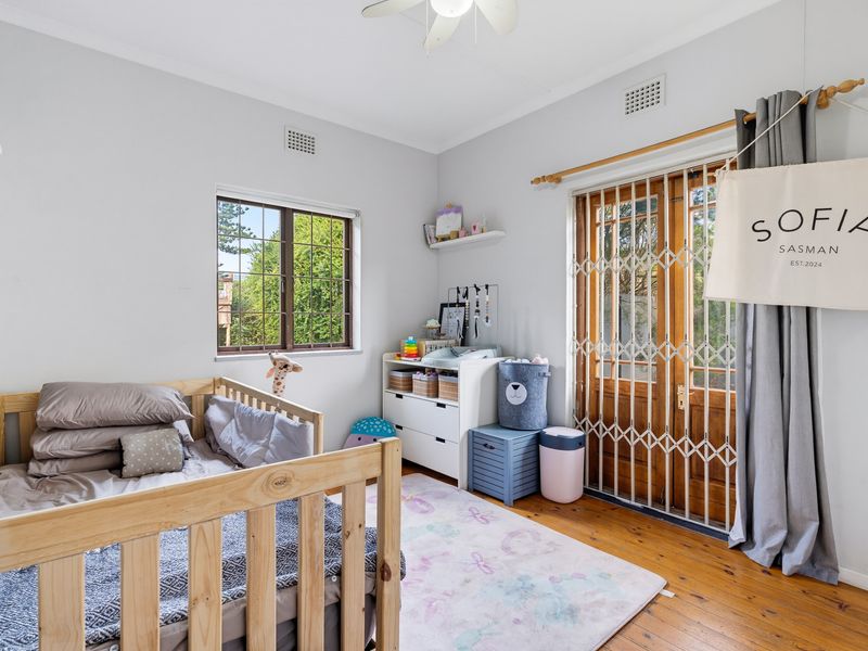 A bright bedroom featuring polished timber flooring, a ceiling fan, and direct access to the outdoors through timber-framed glass doors with security gates.