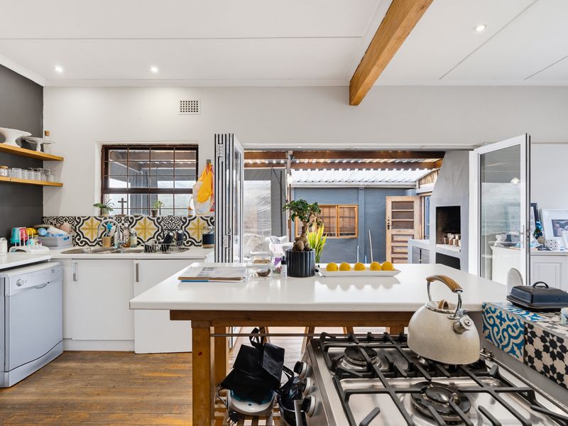 Modern kitchen featuring a gas hob, timber shelving, patterned backsplash, and seamless flow through bi-fold doors to an outdoor patio area with a fireplace.