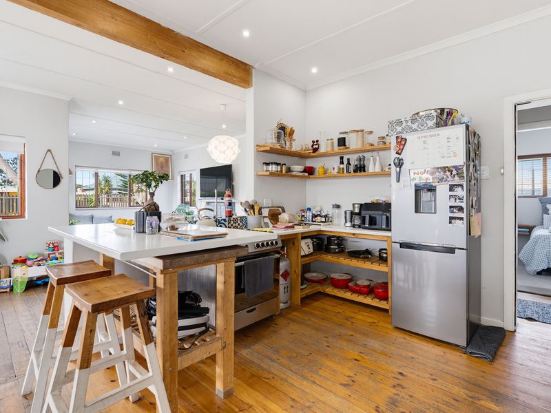 Open-plan kitchen and living area featuring timber flooring, an exposed ceiling beam, a central kitchen island, and custom open shelving.