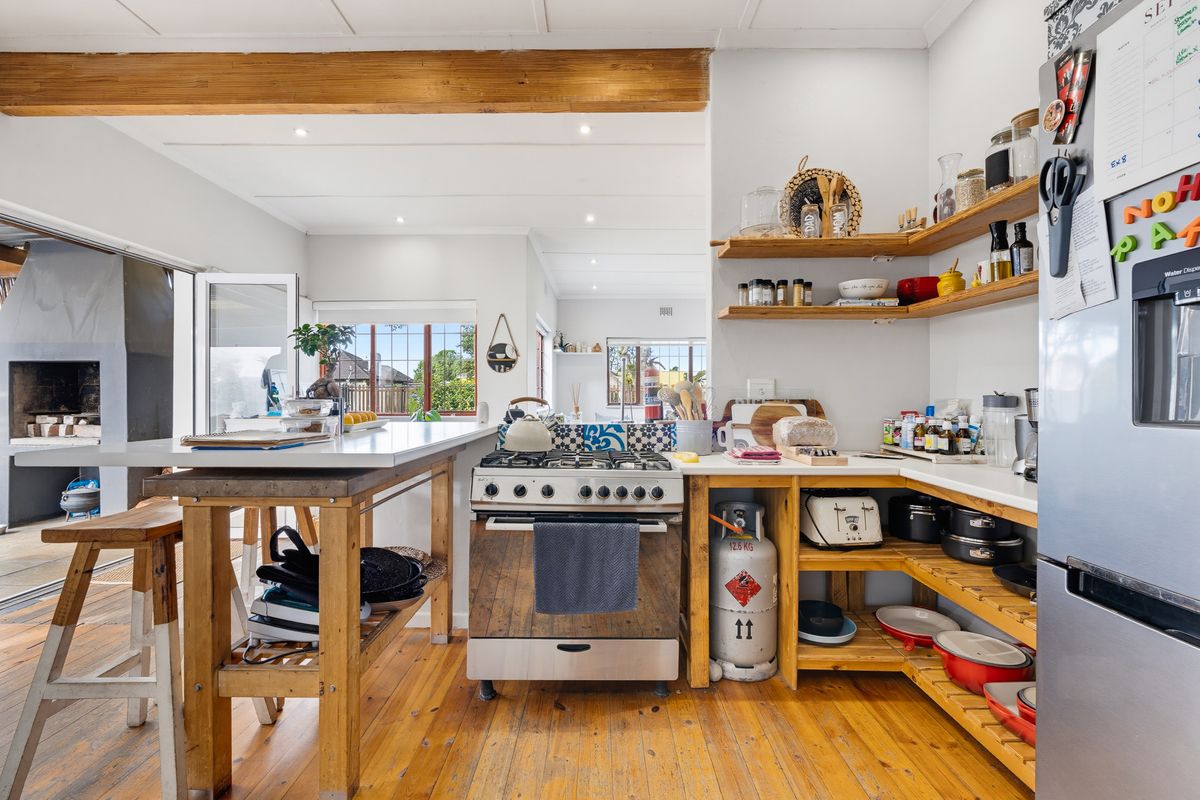 A rustic-style kitchen featuring hardwood flooring, exposed wooden beams, open shelving, and a gas stove with a breakfast counter.