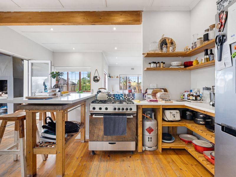 A rustic-style kitchen featuring hardwood flooring, exposed wooden beams, open shelving, and a gas stove with a breakfast counter.