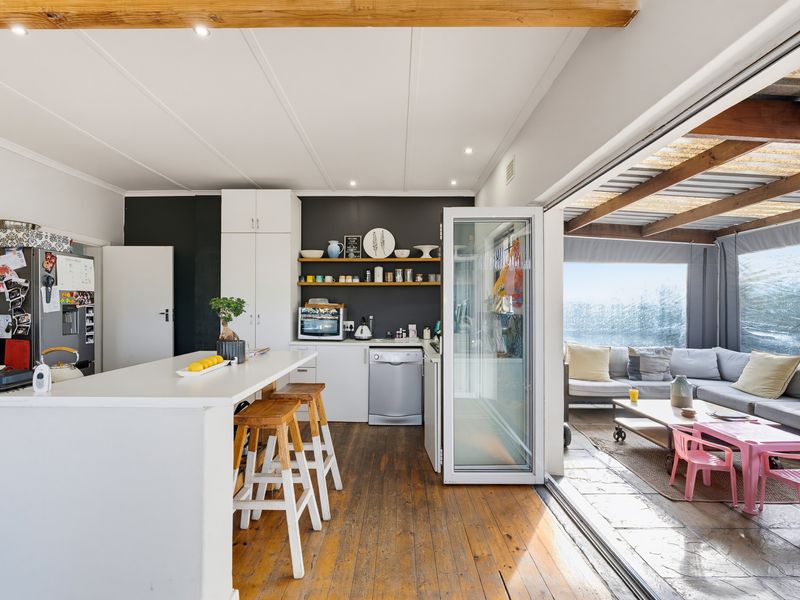 Open-plan kitchen featuring a central island, timber flooring, and exposed ceiling beams, seamlessly flowing through bi-fold doors to an adjoining covered patio area.