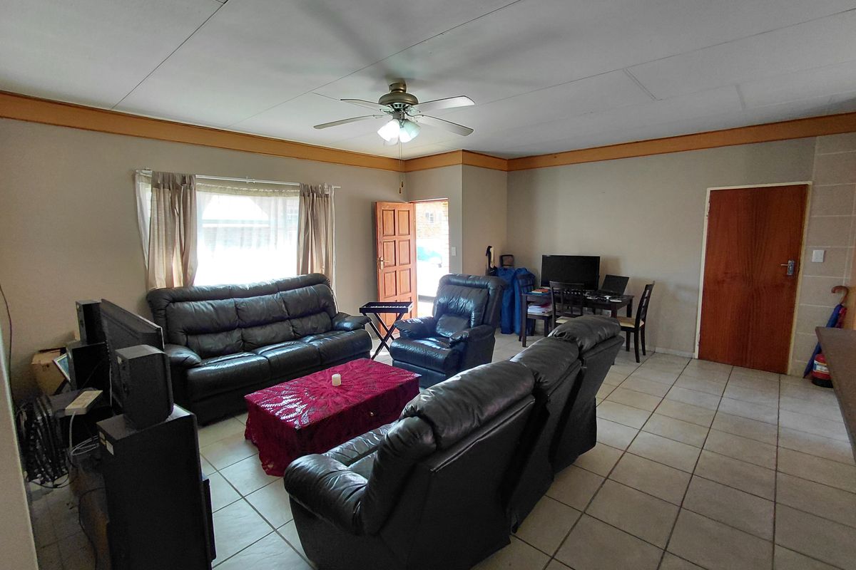 A spacious living room featuring tiled flooring, a ceiling fan, and timber trim details, offering a functional layout with direct access to the entrance.