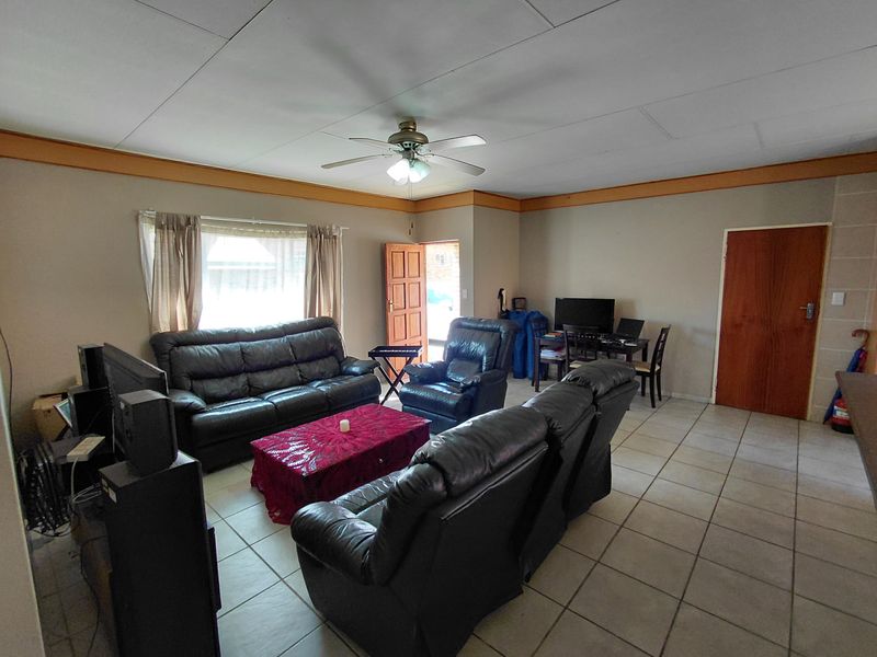 A spacious living room featuring tiled flooring, a ceiling fan, and timber trim details, offering a functional layout with direct access to the entrance.