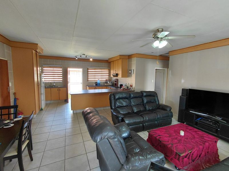 Open-plan living and kitchen area featuring tiled flooring, wooden cabinetry, a kitchen island, and ceiling fan, offering a functional layout for daily living.