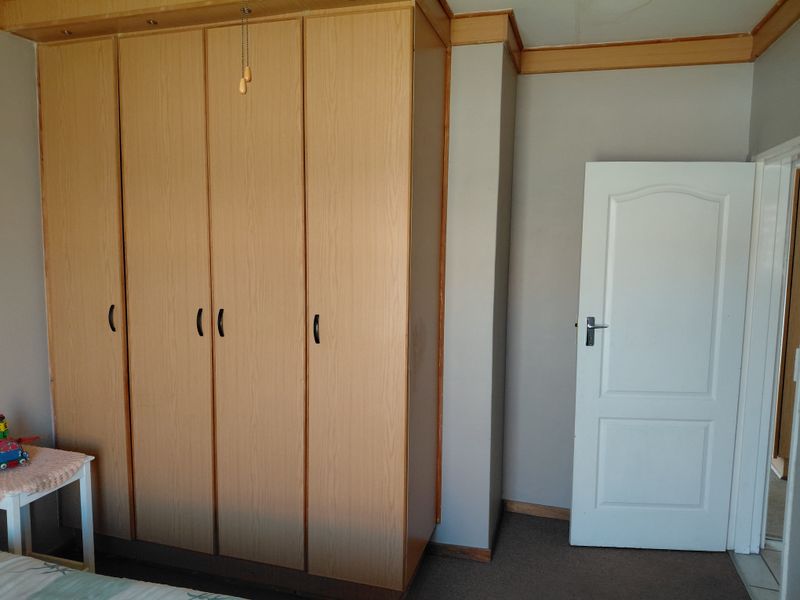 A bedroom featuring a large built-in wooden wardrobe and neutral wall finishes, providing ample storage space.