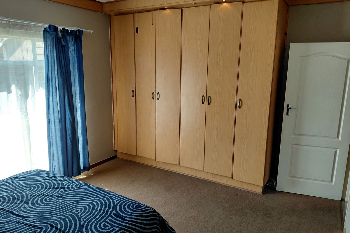 A bedroom featuring extensive light wood built-in cupboards with integrated lighting and carpeted flooring.